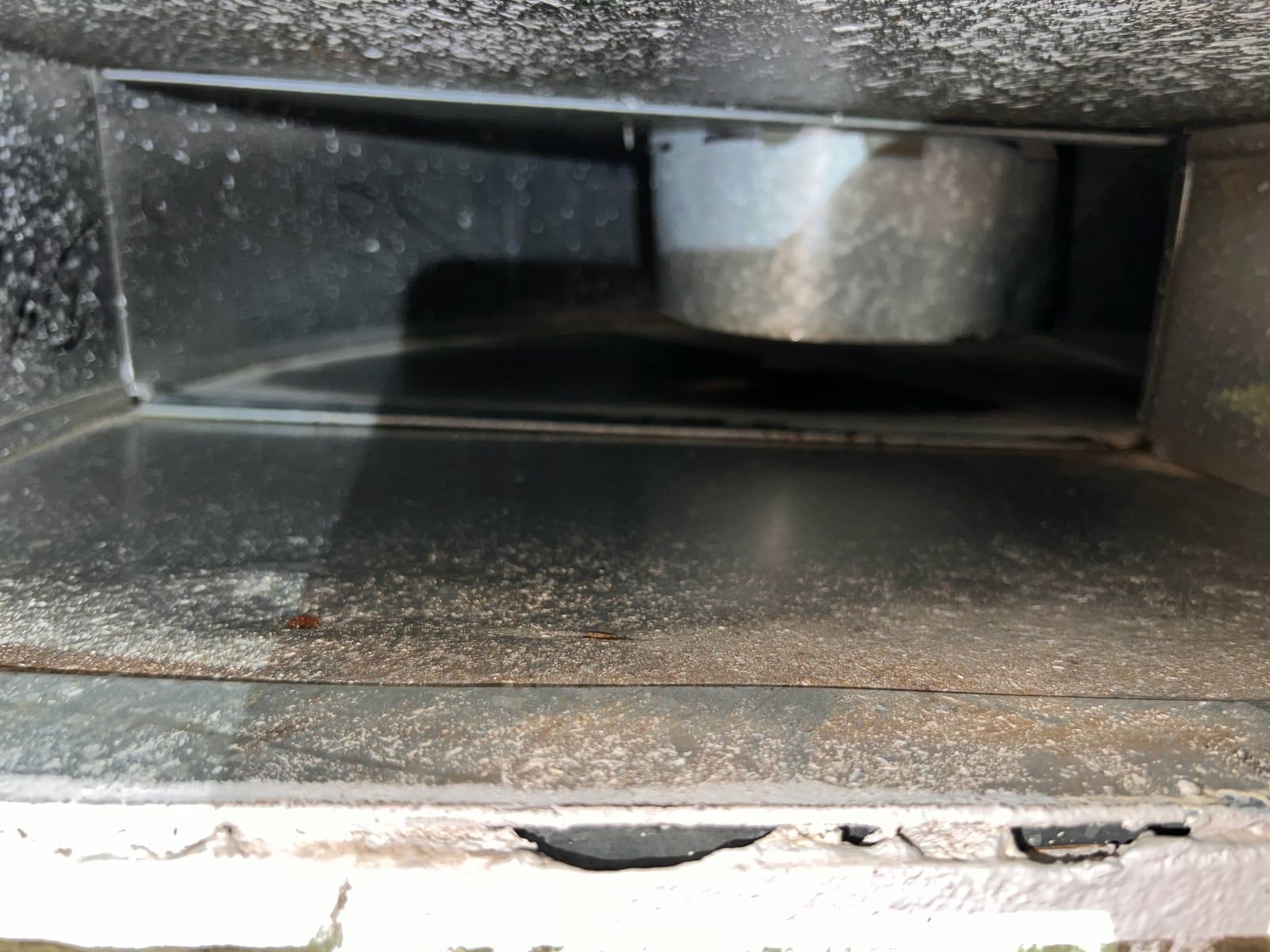 Inside a galvanized supply plenum seen through a register opening, with a round duct takeoff at the back