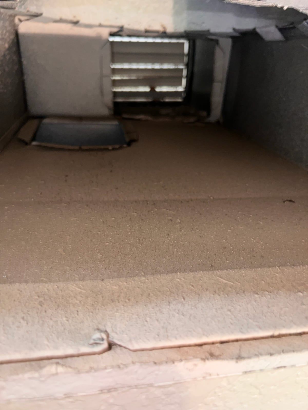Inside a supply duct before cleaning, with a layer of tan dust across the floor of the run