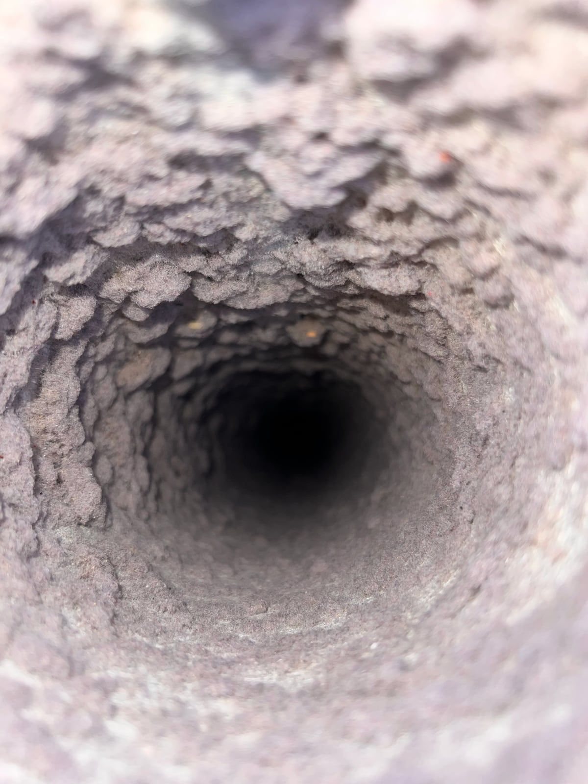 Looking down the inside of a dryer duct whose walls are lined with a thick layer of packed gray lint