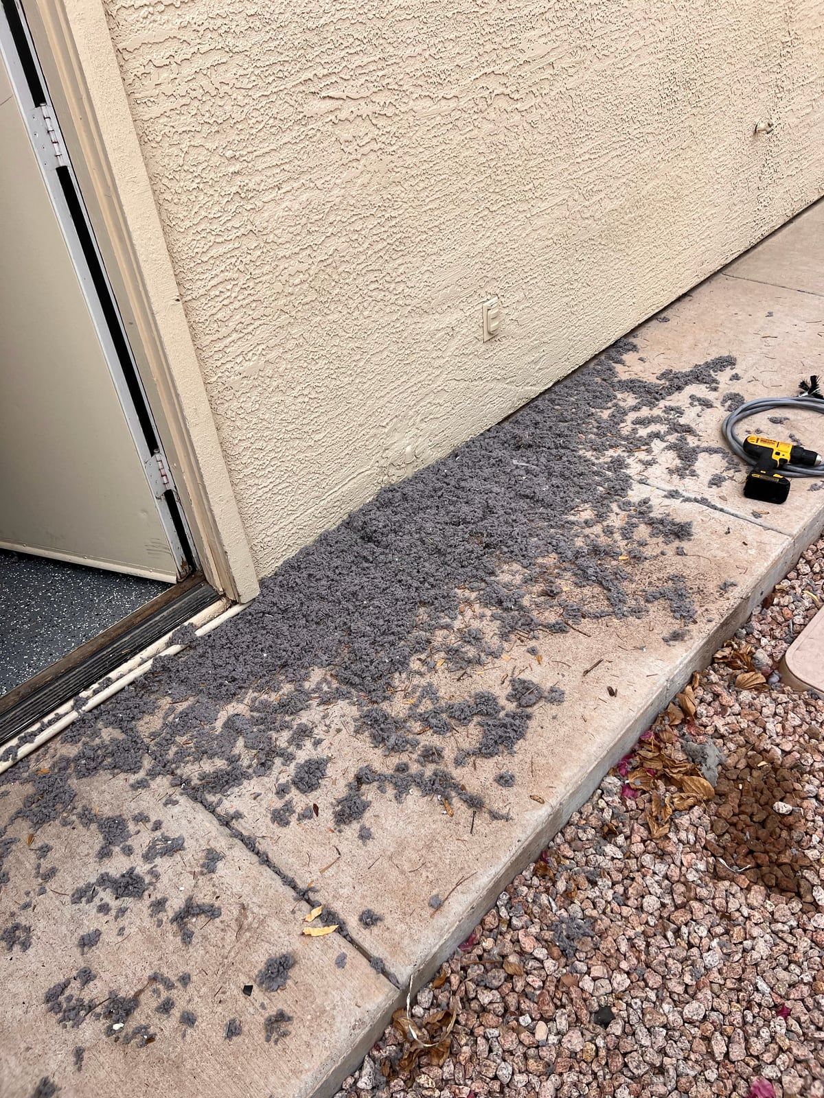 A long trail of gray lint across the concrete along the side of a house, next to an open garage door