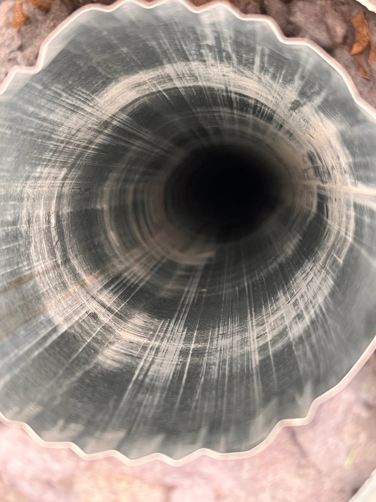 Looking down a brushed metal dryer duct, with pink insulation and loose gray lint around its opening